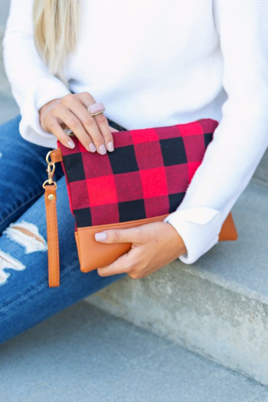 Woman holding buffalo plaid clutch bag with leather wristlet, styled casually with denim.