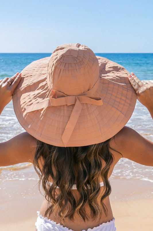 Back view of  a woman wearing white wide-brim sunhat with bow on beach