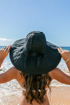 Back view of  a woman wearing white wide-brim sunhat with bow on beach