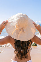 Back view of  a woman wearing white wide-brim sunhat with bow on beach