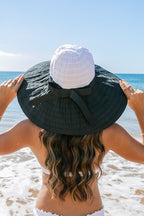 Back view of  a woman wearing white wide-brim sunhat with bow on beach