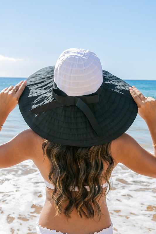 Back view of  a woman wearing white wide-brim sunhat with bow on beach
