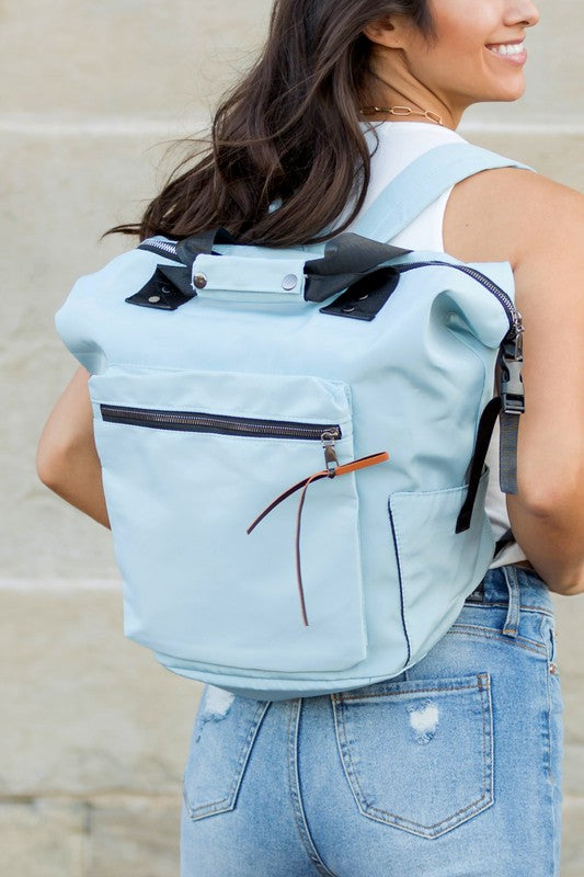 A woman is wearing a backpack. She is dressed in casual clothes and has a smile on her face.