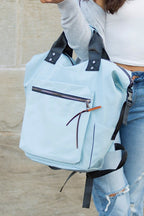 A woman is holding a tote backpack. She is dressed in casual clothes and looks like she is going somewhere. The backpack is a good size for carrying a laptop and other essentials.
