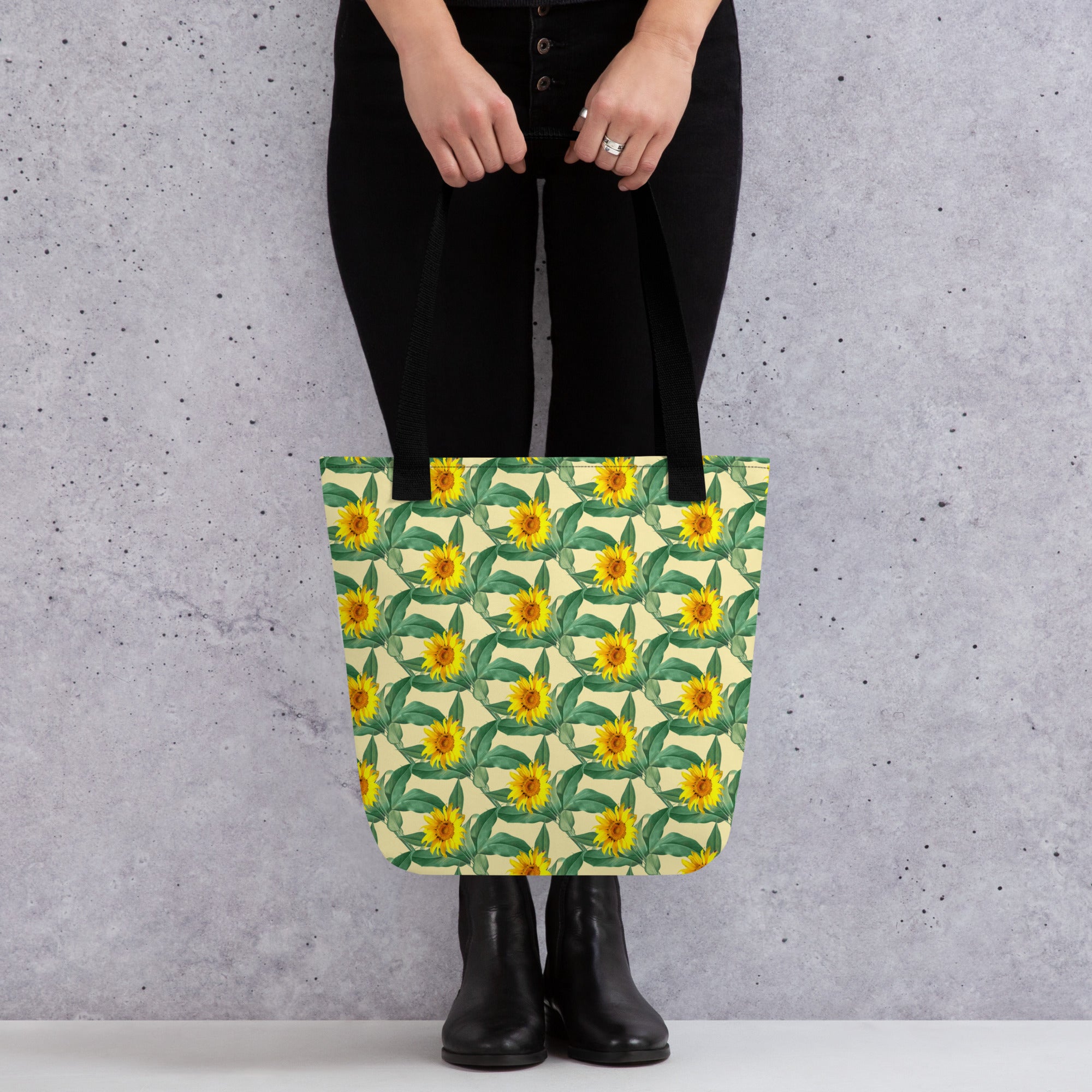 Close-up of sunflower print tote bag with green leaves and yellow flowers held in front of gray background