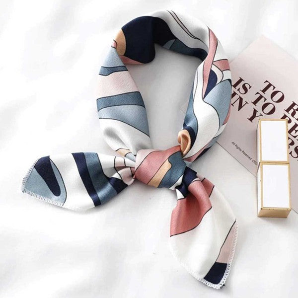 Thiana silk scarf in pink, navy, and white tones styled in a bow with gold accessory nearby